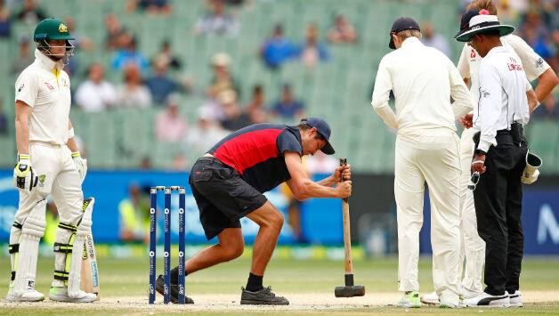 Steve Smith of Australia and bowler Stuart Broad of England look on as the groundsman tries to flatten the bowlers foot marks on the pitch © Getty Images